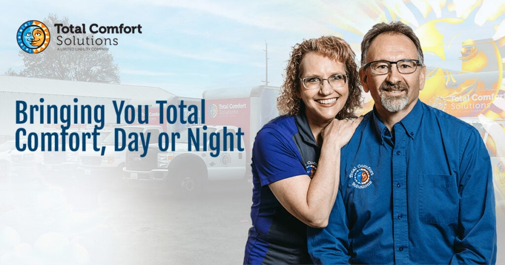 Two smiling Total Comfort Solutions technicians in blue uniforms standing in front of service truck. Text reads 'Bringing You Total Comfort, Day or Night.'